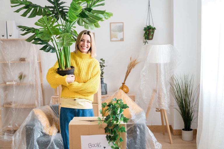 A woman holding a Monstera while unpacking boxes in her new home